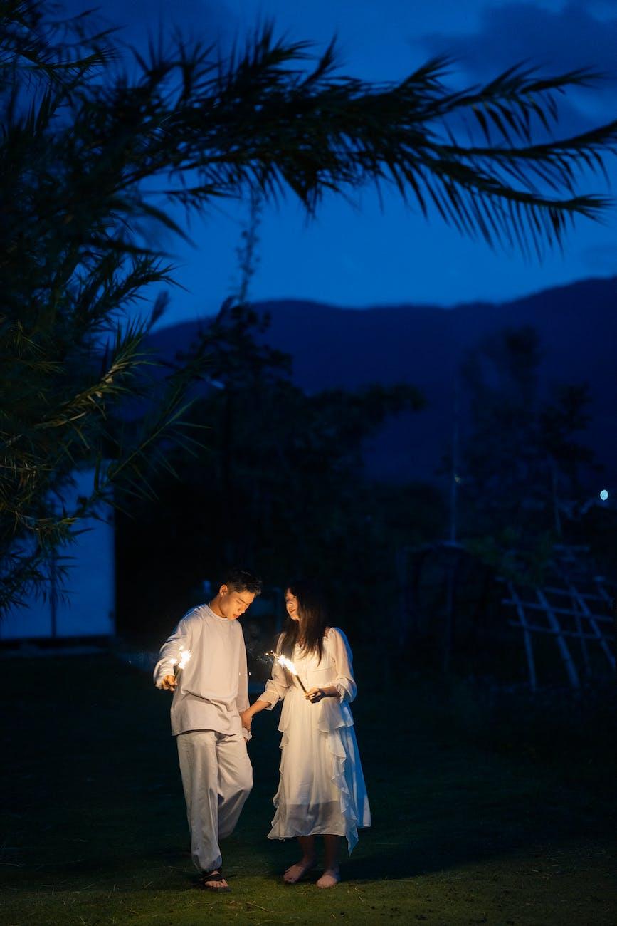man and woman in white clothes walking outside with candles